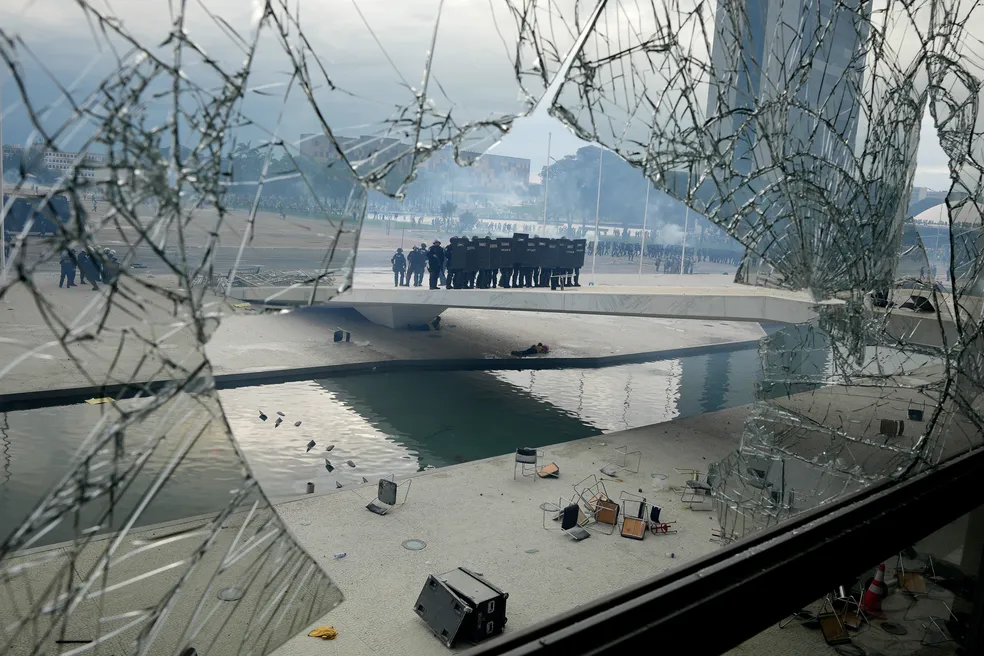 Policiais sobem a rampa do Palácio do Planalto vistos através de uma janela quebrada por vândalos durante invasão em Brasília em 8 de janeiro. - Foto: Eraldo Peres/AP